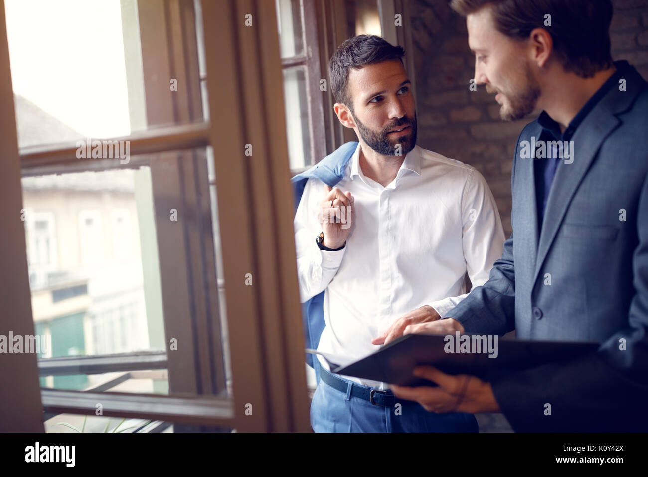 Two young businessmen in office standing near window and talking Stock ...