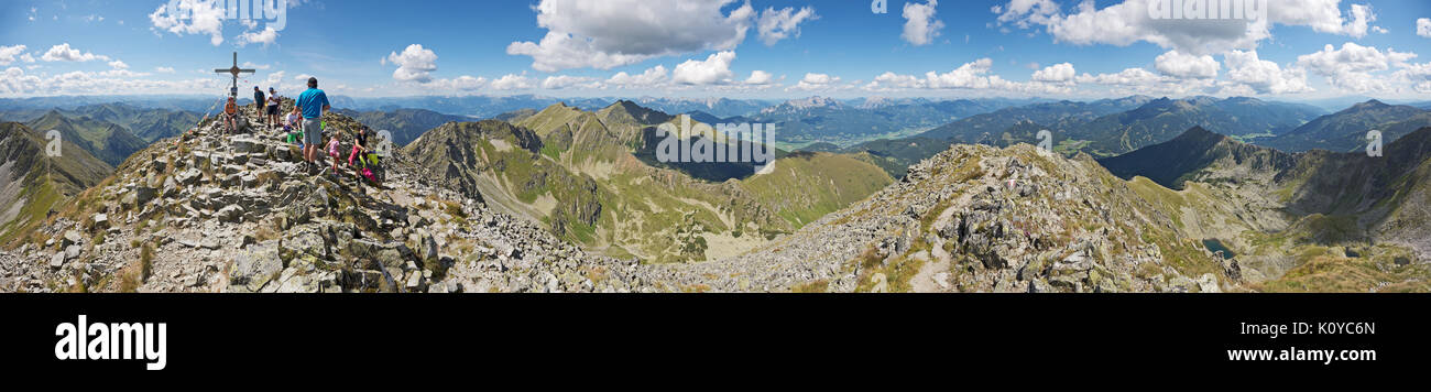 Panoramic view from rocky mountain peak Boesenstein, Austria. Hikers enjoying fantastic clear views over high alpine landscape under cloudy blue sky. Stock Photo