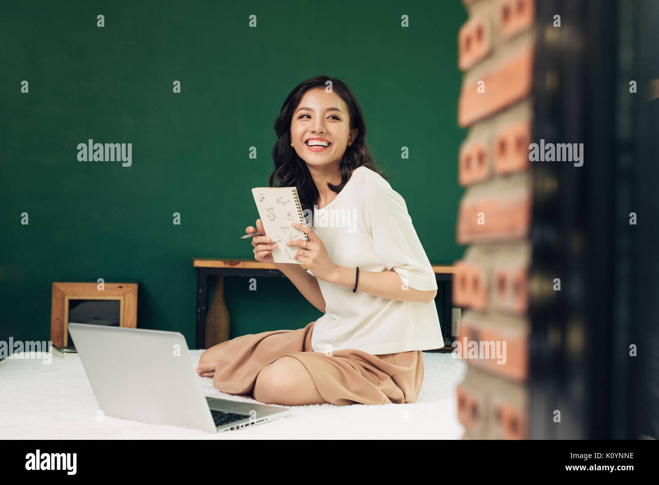 Beautiful young smiling woman working on laptop while sitting on bed at ...