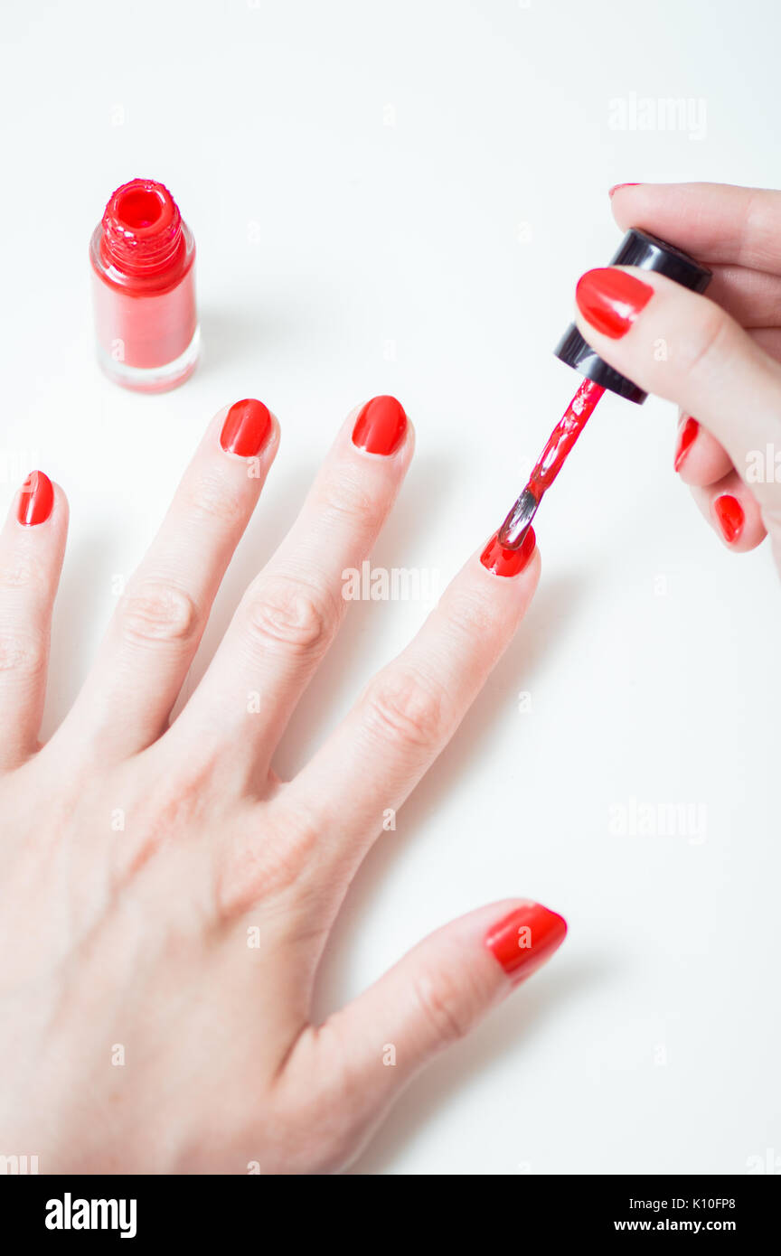 Young woman is painting her nails with red nail polish Stock Photo