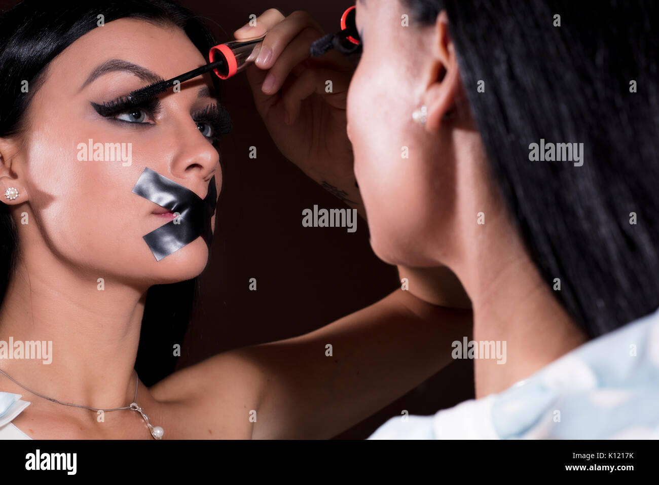 Woman applying makeup on with tape on her mouth Stock Photo