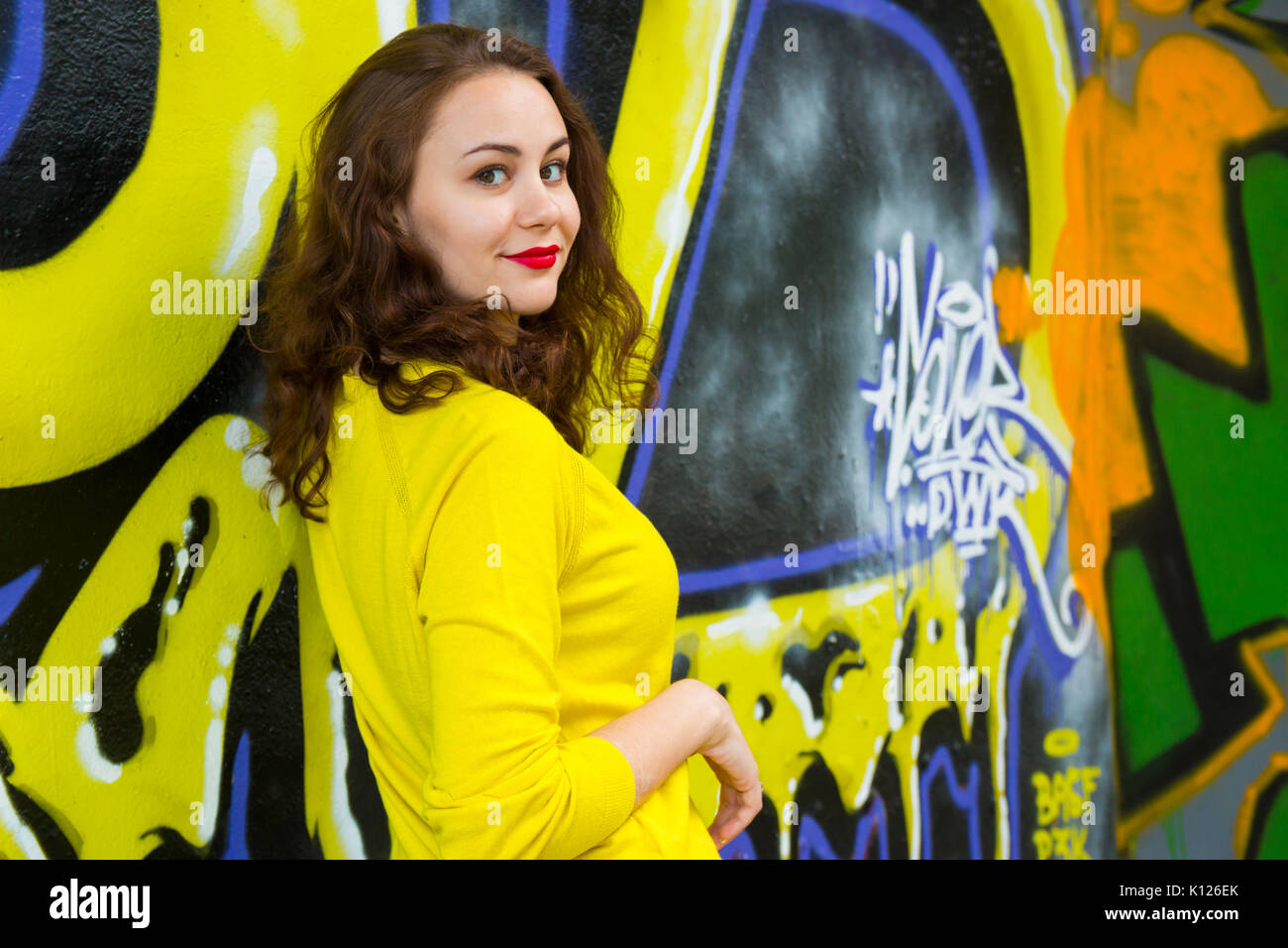 Portrait of cute girl in yellow pullover on graffiti wall background Stock Photo