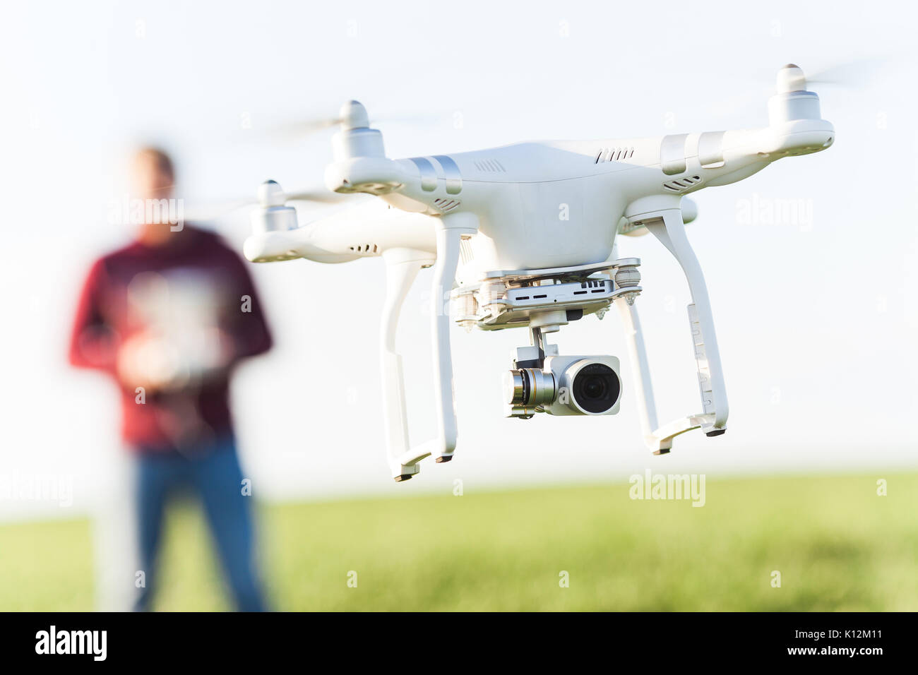 RUSSIA, ROSTOV-ON-DON - APRIL 20, 2017: closeup on superb white high-tech drone at low altitude, at background is a male pilot in jeans and fleece hoo Stock Photo