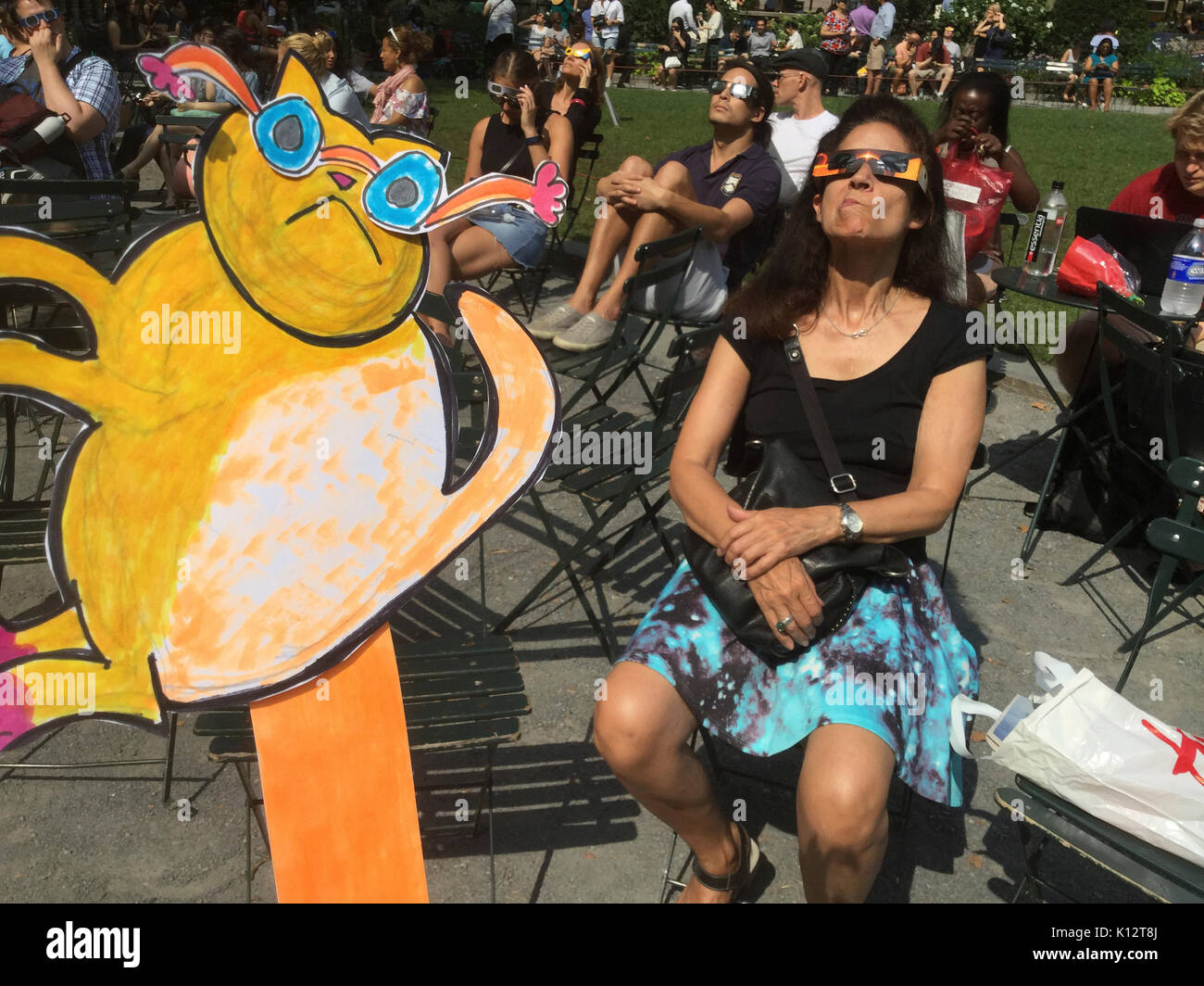 Thousands of the curious congregate in Bryant Park to watch the partial solar eclipse occurring in New York on Monday, August 21, 2017. New York City is not in the path of totality with the moon covering only almost 72 percent of the sun during the 2:44PM peak.  Eclipse Kat, drawn by Frances M. Roberts joins the crowds to watch the eclipse.  (© Frances M. Roberts) Illustration Stock Photo