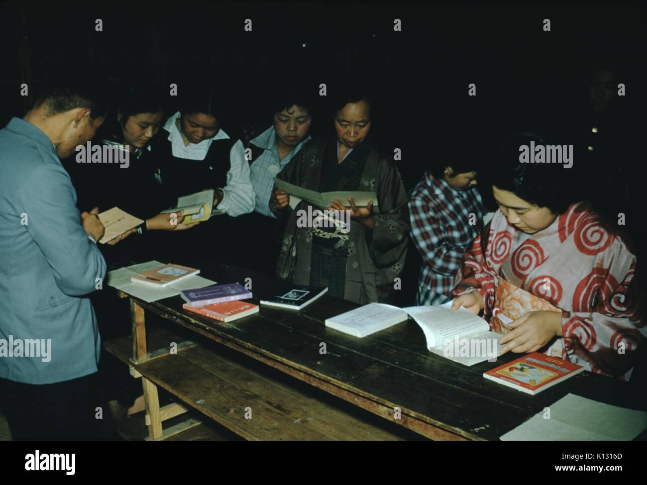 Japanese churchgoers reading prayer books at a mission church, the women wearing decorative kimonos, all with looks of concentration, Japan, 1952. Stock Photo
