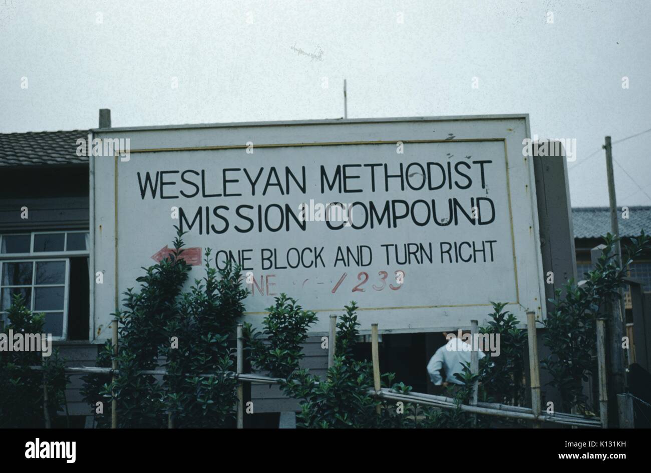 Sign for the Wesleyan Methodist Mission Compound, man standing in front of the sign with hands on his hips, Japan, 1952. Stock Photo