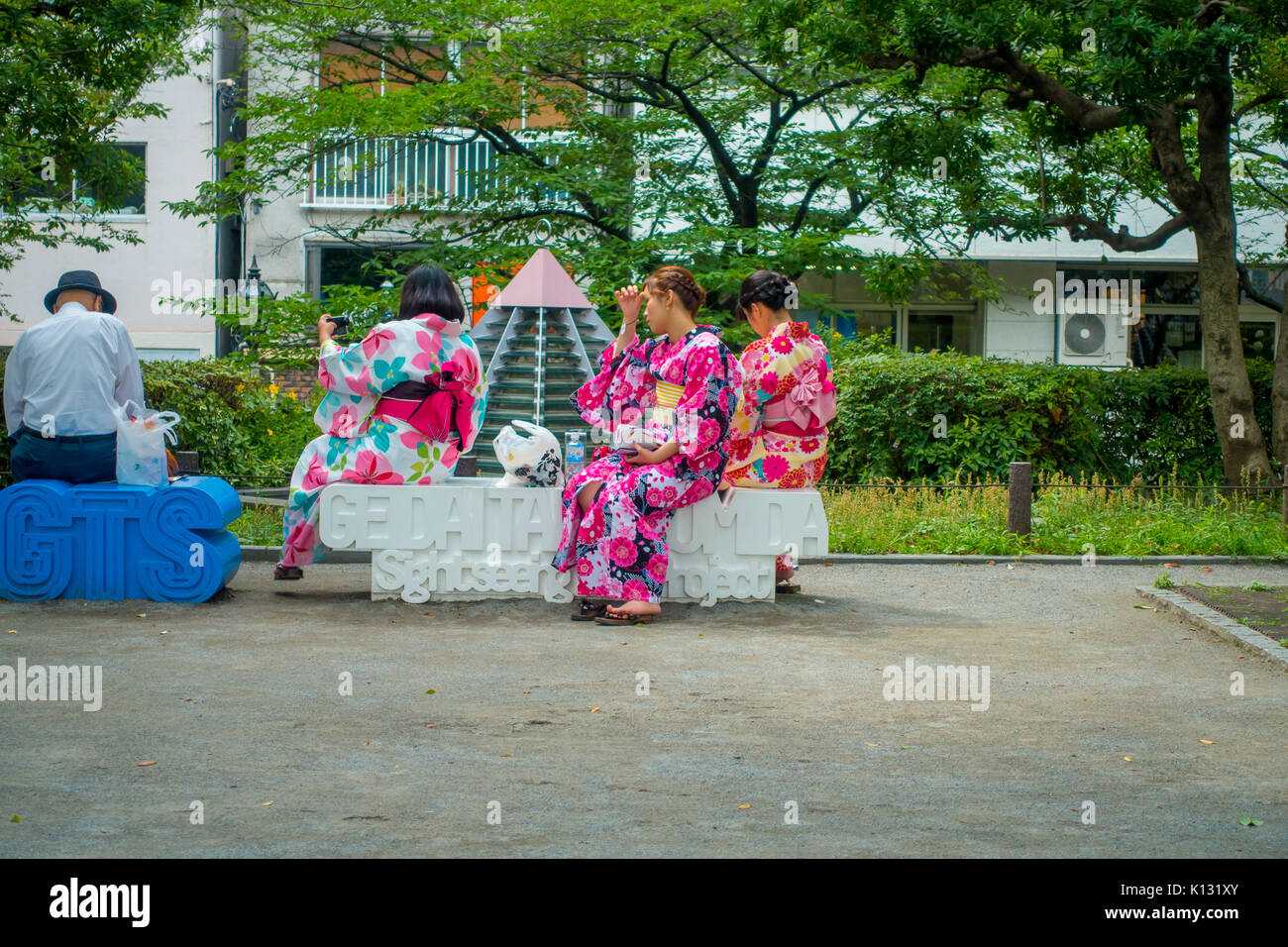 TOKYO, JAPAN JUNE 28 - 2017: Unidentified group of women wearing a kimono dress and taking selfies to theirself, sitting in a white public chair in a park near of the Buddhist Temple Sensoji in Tokyo, Japan. The Sensoji temple in Asakusa area is the oldest temple in Tokyo Stock Photo