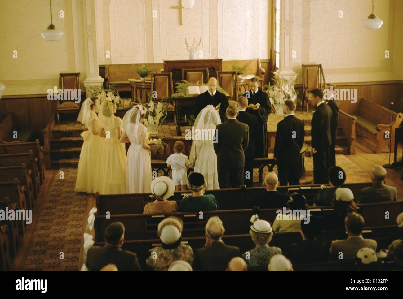 Wedding at a missionary church, bridal party, bridge and groom standing in the front of the church with the pastor, high-angle view, attendees sitting in pews and wearing formal outfits, Japan, 1943. Stock Photo