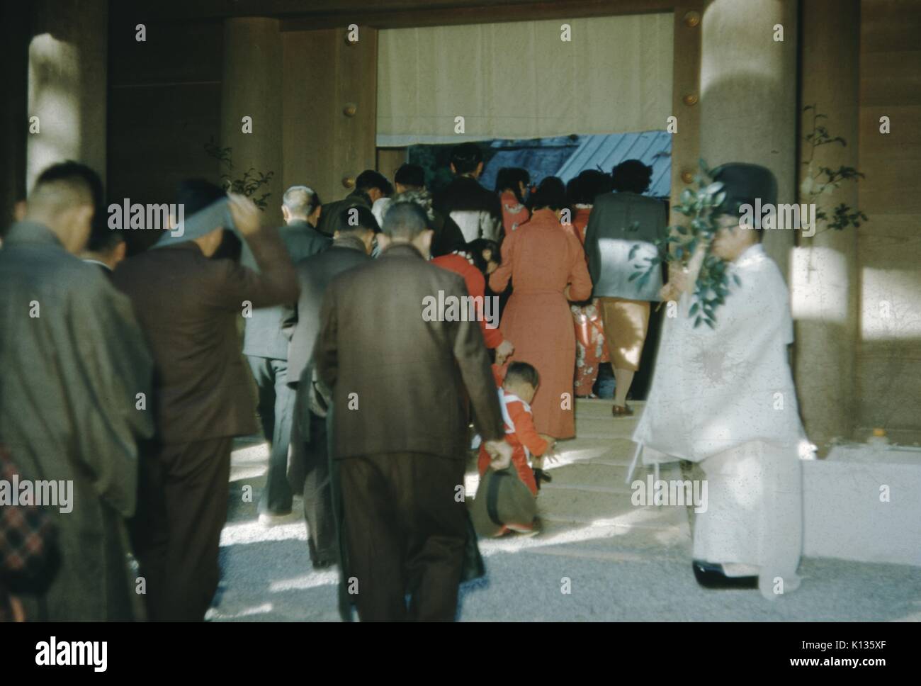 Japanese churchgoers with bowed heads and modest clothing walking in a line and entering a church, Japan, 1951. Stock Photo