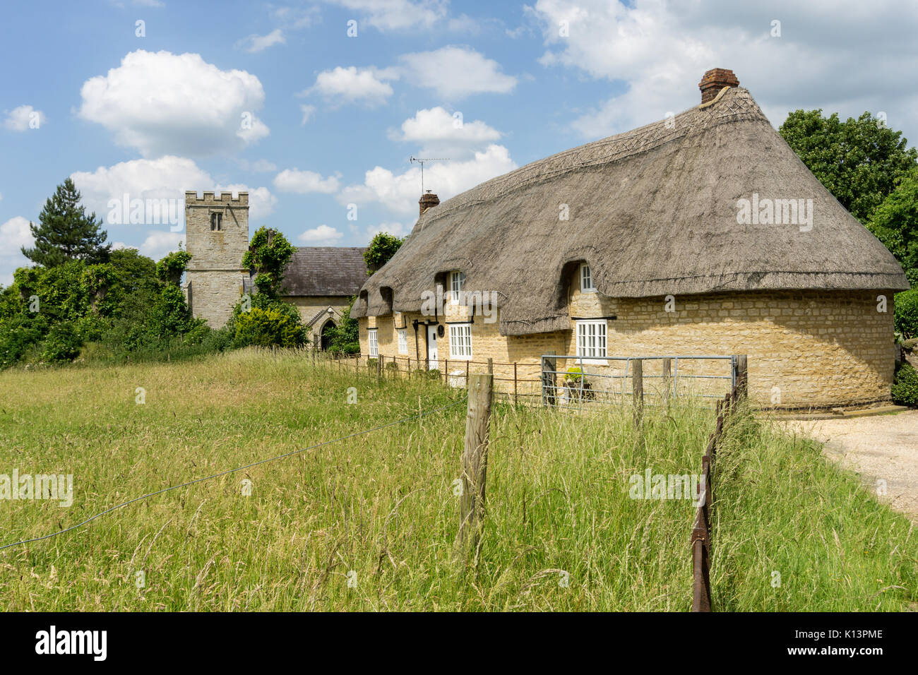 Thatched house with a church in the background, a quintessential English scene from the village of Alderton, Northamptonshire, UK Stock Photo