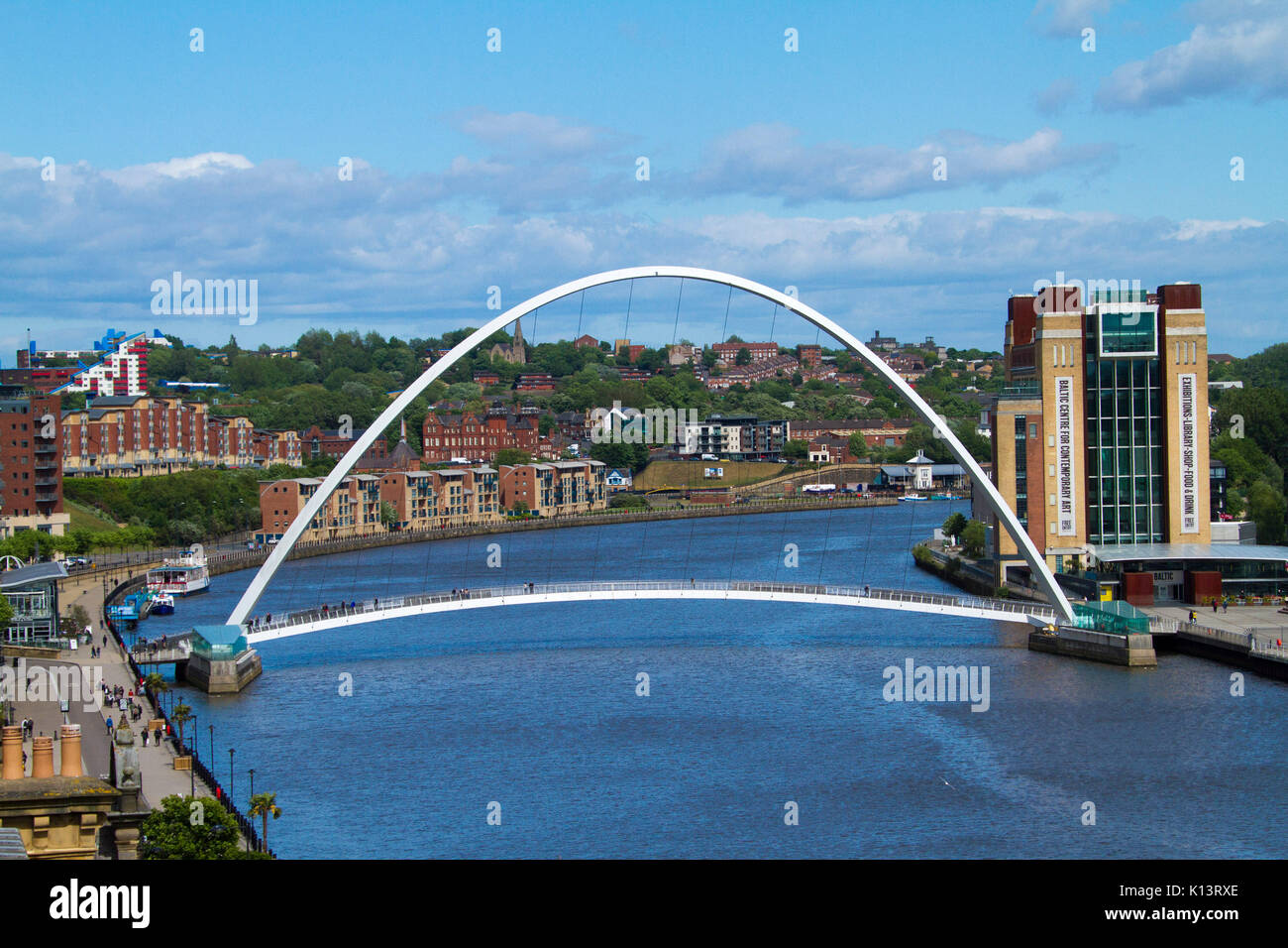 Gateshead millennium bridge, tilting pedestrian bridge across Tyne River at Newcastle-upon-Tyne with buildings of city nearby under blue sky Stock Photo