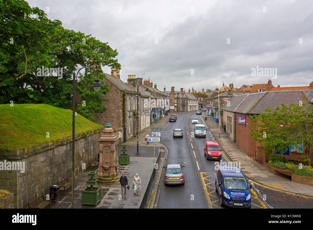Main street of Berwick-upon-Tweed slicing through town of historic buildings, with vehicles and pedestrians passing old Roman wall, in England Stock Photo