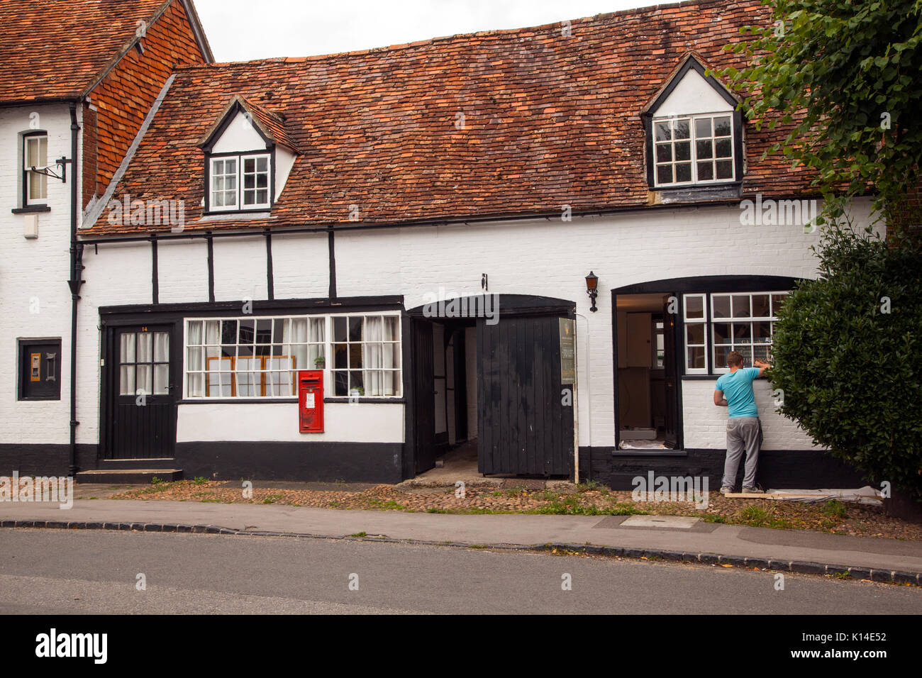 Man painting the windows of the old post office in the high street Dorchester on Thames Oxfordshire an old black and white building Stock Photo