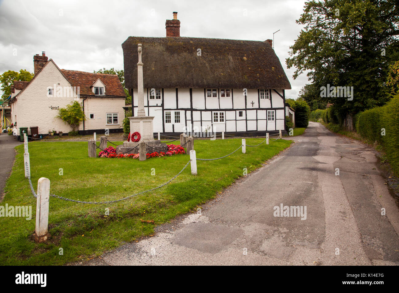War memorial standing on the village green  with black and white halve timbered house with thatched roof behind  at Dorchester on Thames Oxfordshire Stock Photo