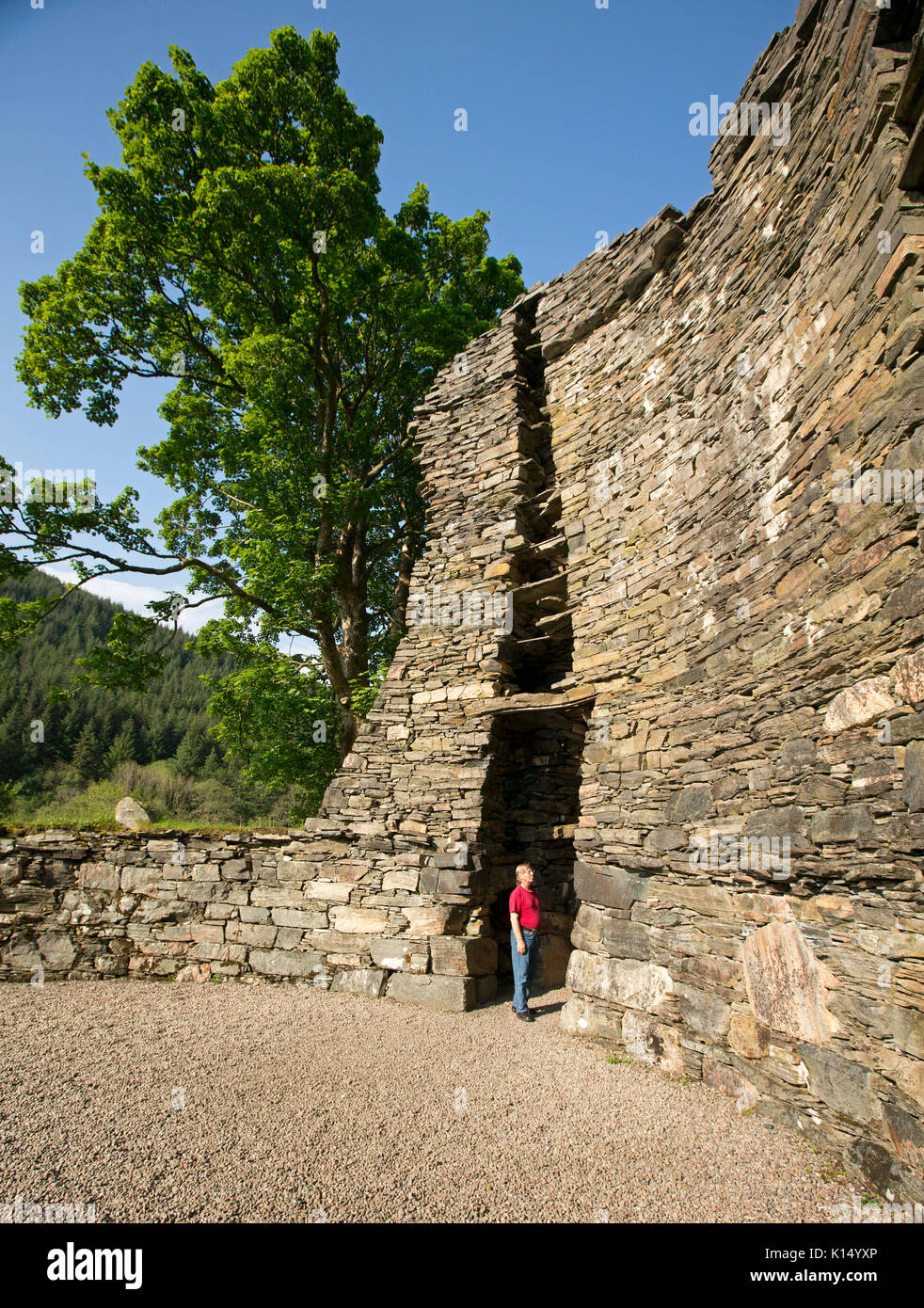 Imposing remains of ancient Dun Telve broch, dry stone Iron Age roundhouse in Scotland, with man standing in doorway to show its immense height Stock Photo