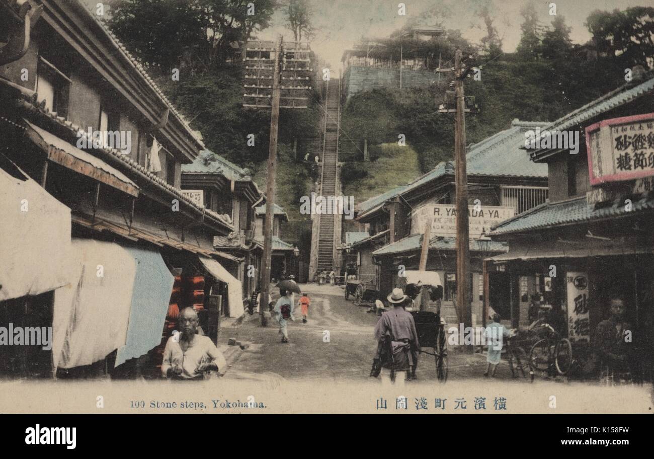 A postcard created from a tinted photograph, people are shown walking along a street lined with businesses, at the end of the street is a single, extremely tall staircase consisting of 100 stone steps scaling the entire face of a hill, two buildings are seen at the top of the hill, Yokohama, Japan, 1912. From the New York Public Library. Stock Photo
