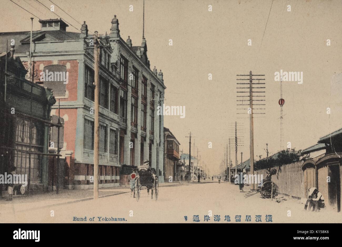 A postcard created from a tinted photograph, buildings are European style and the road is lined with utility poles, people can be seen on carts and on the street, in a European district called the bund, Yokohama, Japan, 1912. From the New York Public Library. Stock Photo