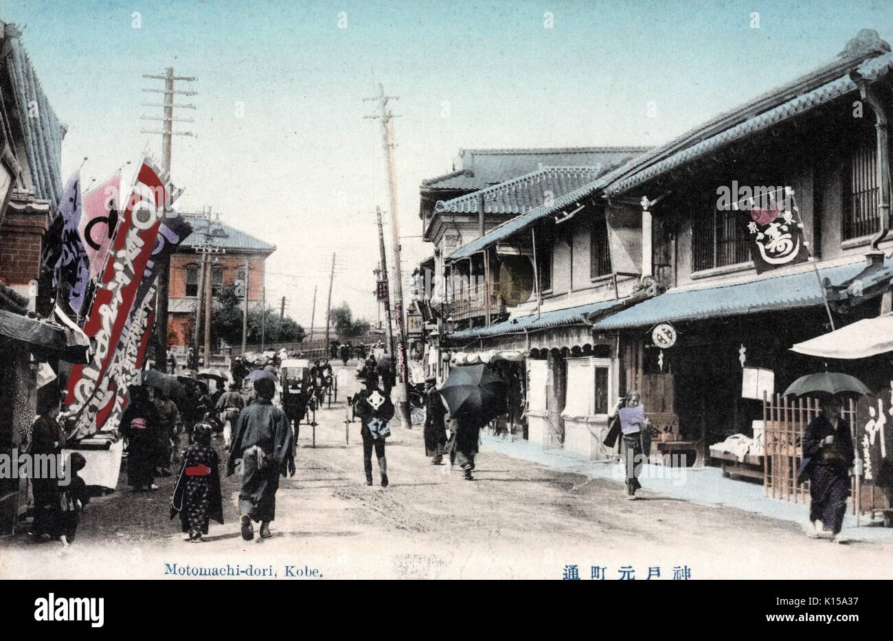 Hand colored post card of Motomachi-dori, showing people and carts on a road lined with stores, Kobe, Japan, 1912. From the New York Public Library. Stock Photo