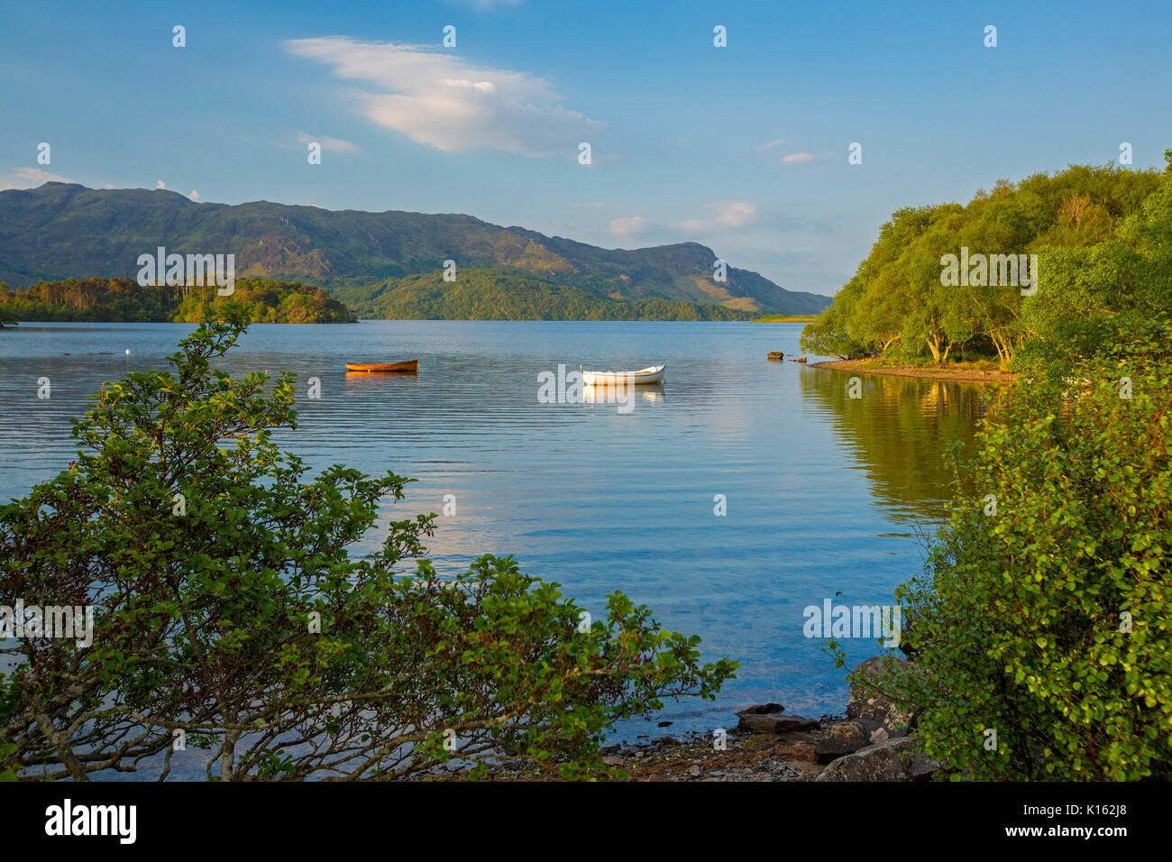 Stunning landscape with Loch Morar hemmed with rugged mountains and with boats on calm blue water under blue sky in Scotland Stock Photo