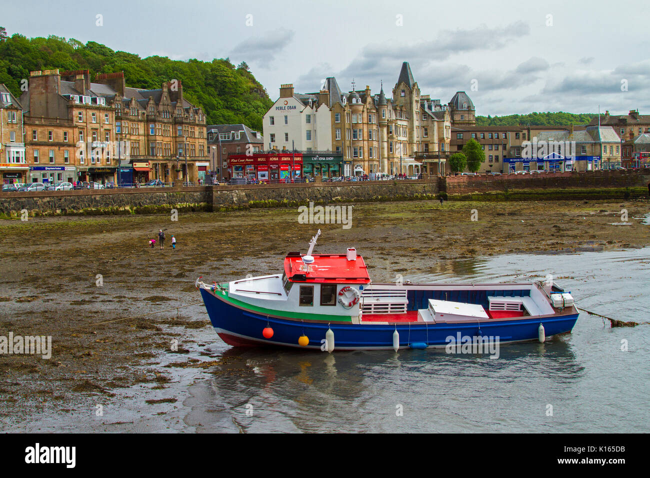 Scottish town of Oban with row of waterfront buildings with boat  in harbour at low tide in foreground Stock Photo