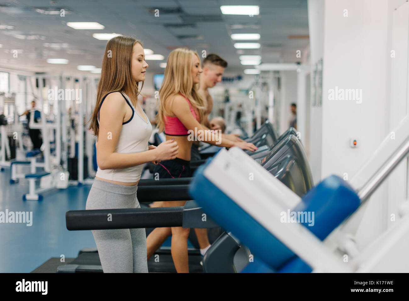 group of young people running on treadmills in gym. Blonde girl set a pace of her running. Stock Photo