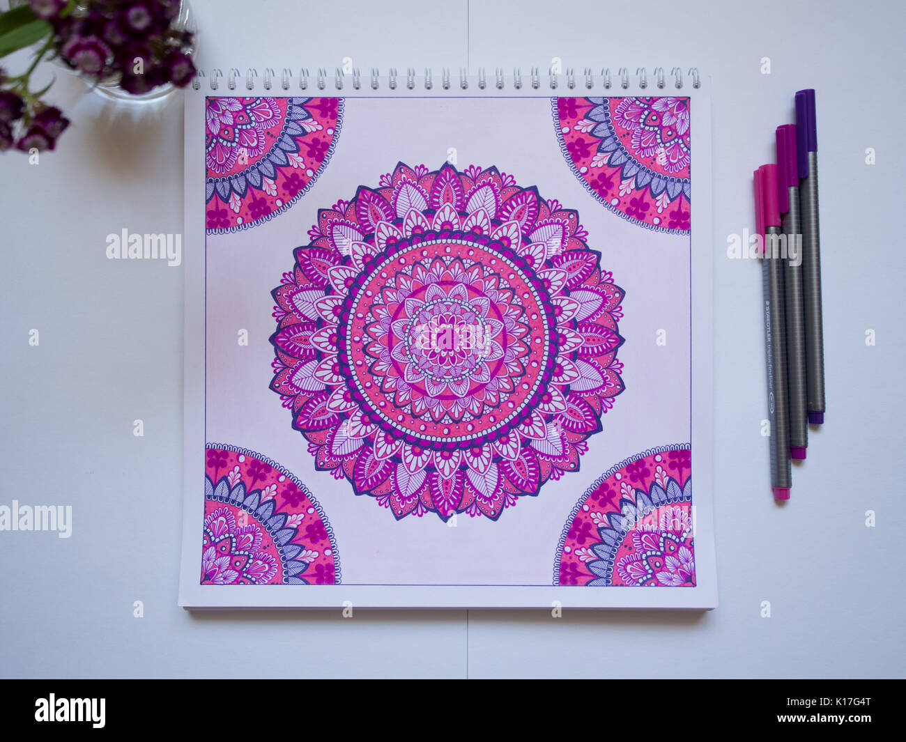 Concept photo of the pens and a sketchbook with a picture of a pink handmade mandala Stock Photo