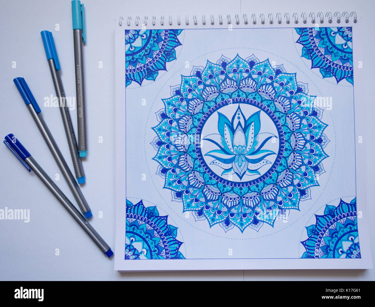 Concept photo of the pens and a sketchbook with a picture of a blue handmade mandala Stock Photo