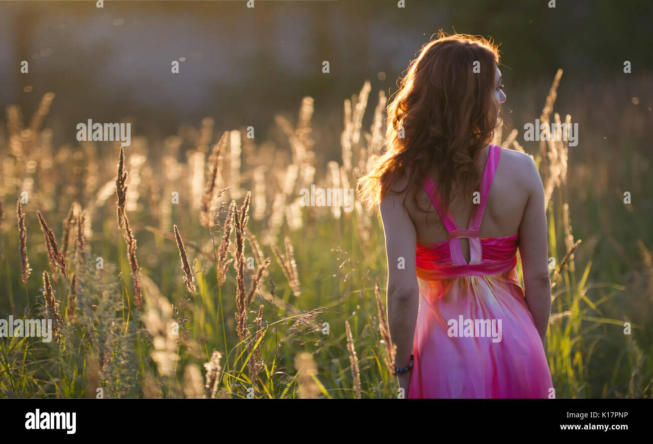 Attractive young woman walking on meadow at sunset - rear view Stock ...