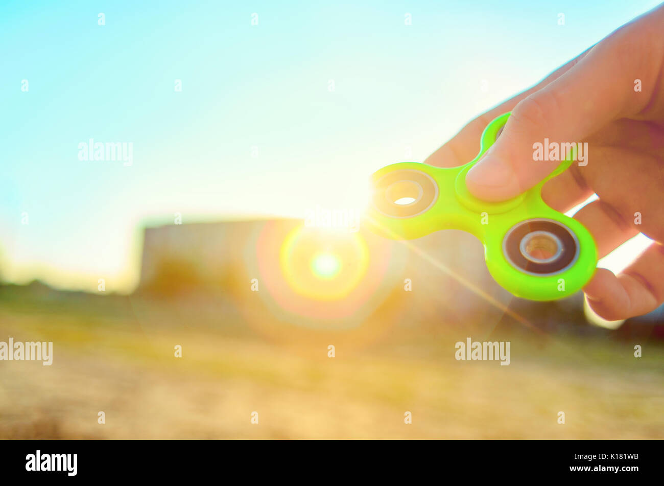 Teenager hand holding trendy antistress gadget fidget spinner. Man playing  with green spinner outdoors on the bright bokeh sunlight rays. Shallow DOF  Stock Photo - Alamy