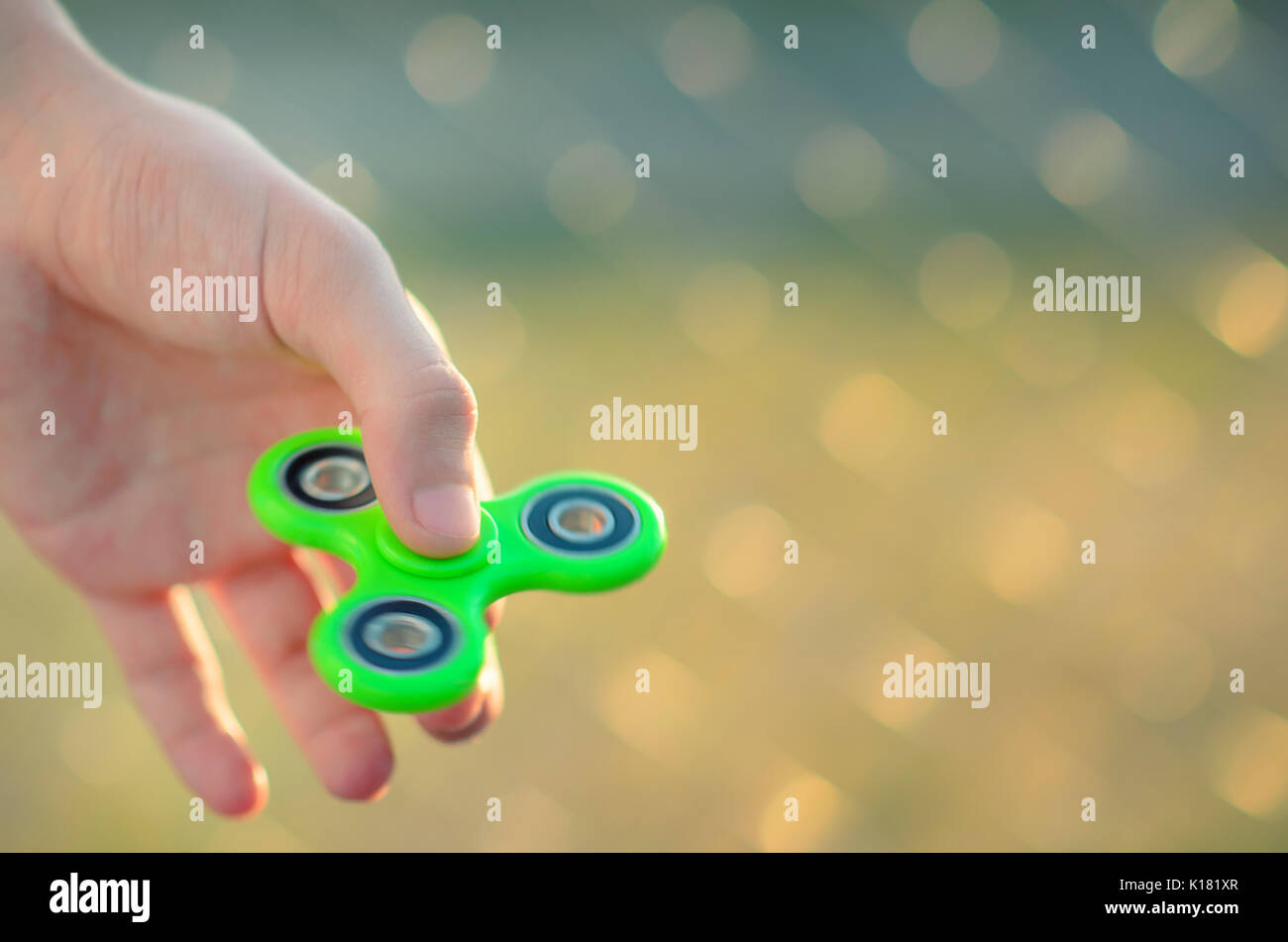 Guy hand holding modern relaxing gadget fidget spinner. Teenager playing  with green spinner outdoors on the rabitz grid bokeh. Shallow DOF Stock  Photo - Alamy