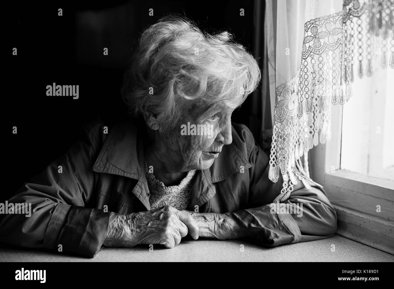 An elderly woman looks longingly out the window. Stock Photo