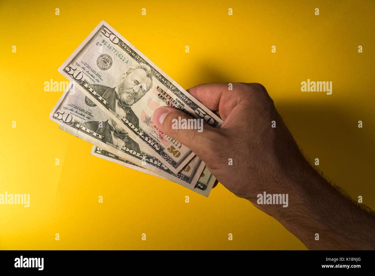 A man's hand holds out dollars. Hand and money on a yellow background. Stock Photo
