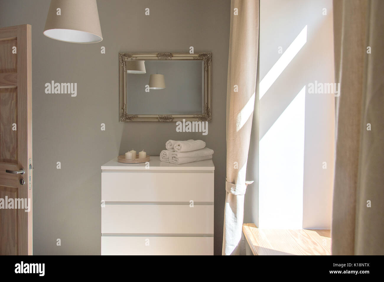 Scandinavian style interior design of a small bedroom with a white chest of drawers, mirror, hanging lamps and light coming through the window Stock Photo