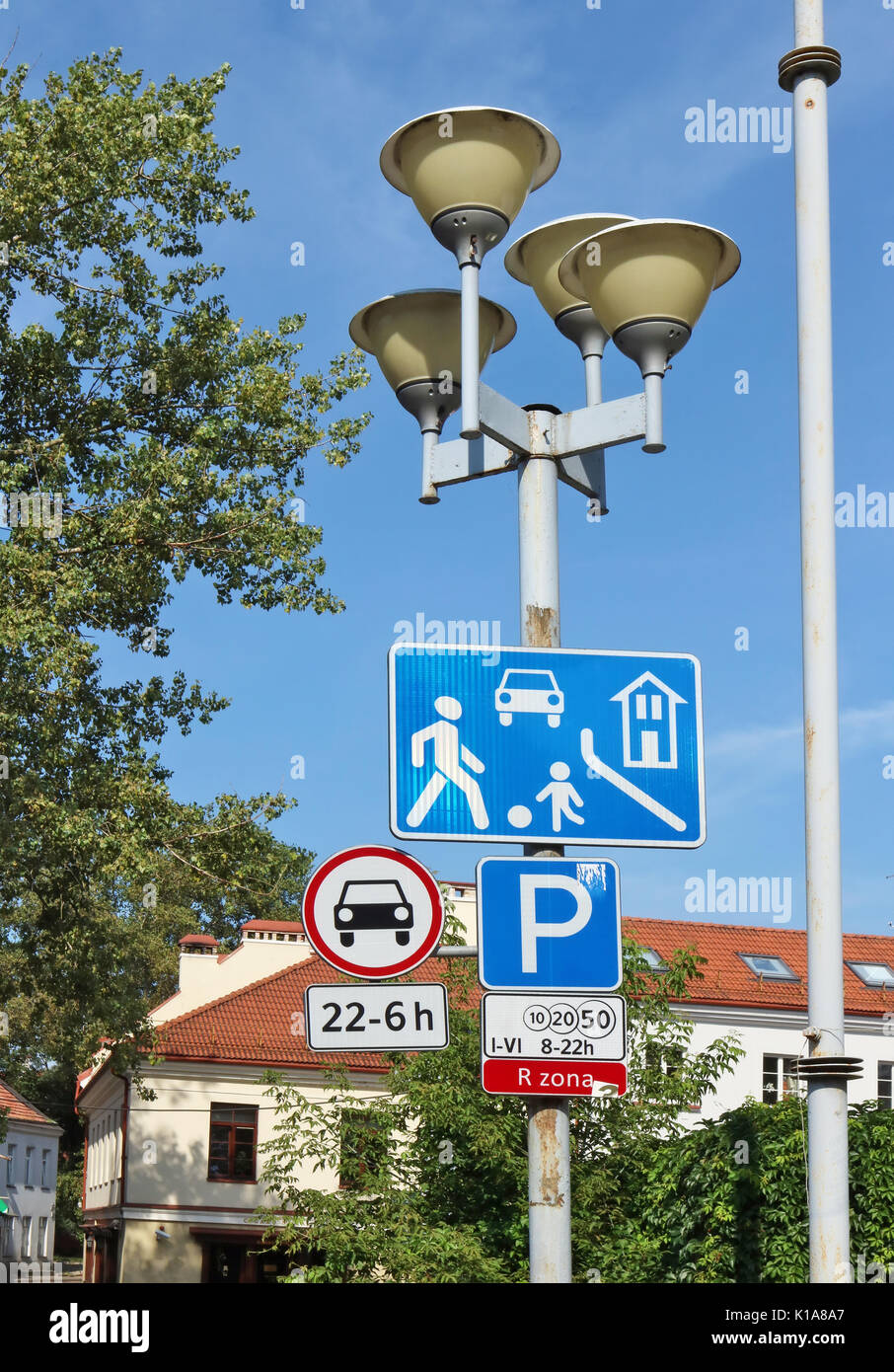 Road signs of the red urban automotive zone hang on a street lamp