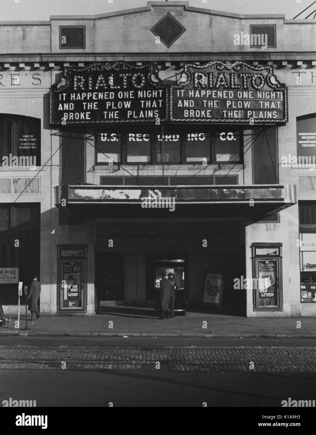 Two men purchasing tickets to attend a movie at a Rialto Theatre, showing It Happened One Night and The Plow That Broke the Plains, a third man looks on, Washington, DC, 1936. From the New York Public Library. Stock Photo