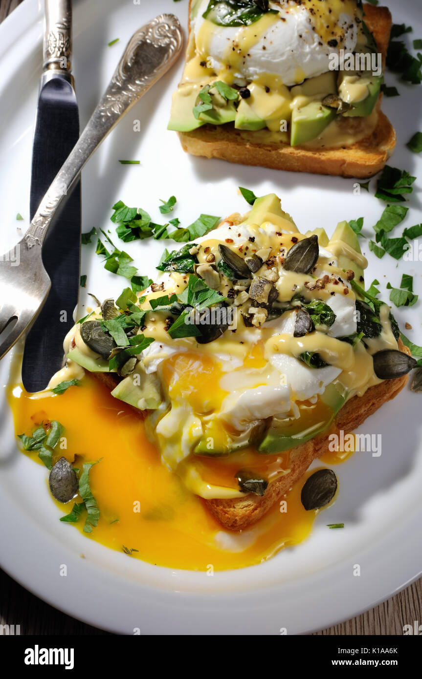 Eggs Benedict on toast with Dutch sauce, slices of avocado Stock Photo