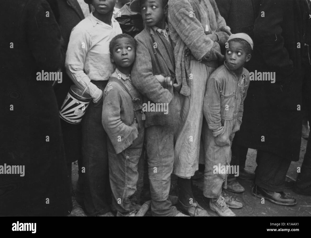Three African-American children standing in line with other flood refugees, children and adults, for mealtime, Forrest City, Arkansas, 1937. From the New York Public Library. Stock Photo