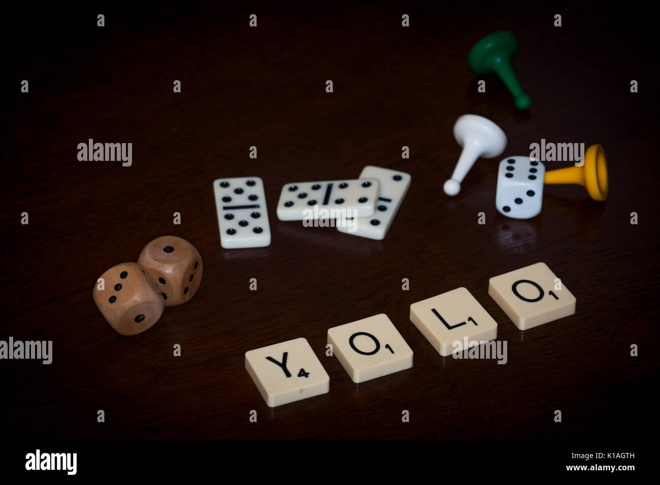 Word tiles spell out 'YOLO' (You only live once), various board gaming paraphernalia is close by. Stock Photo