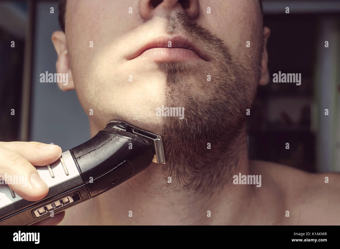 Young bearded man during grooming of beard using trimmer. Half face with a beard half shaved. Stock Photo