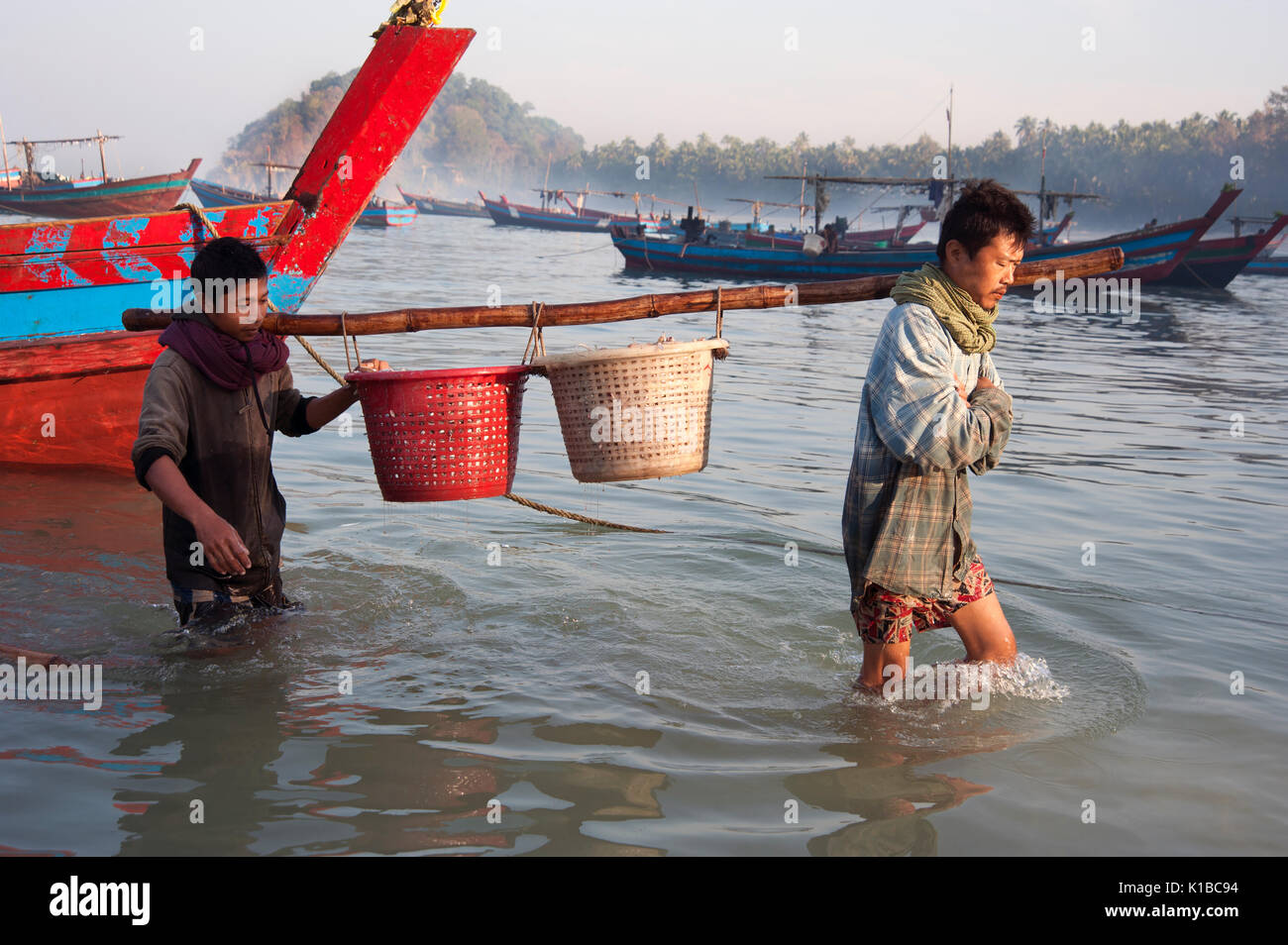 Burmese fishermen bring ashore baskets of fish onto Ngapali beach Myanmar at dawn Stock Photo