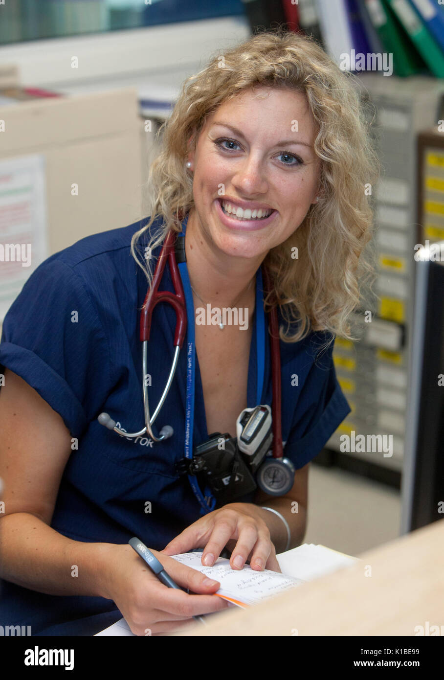 A doctor smiles in a busy ward at an NHS Hospital Stock Photo
