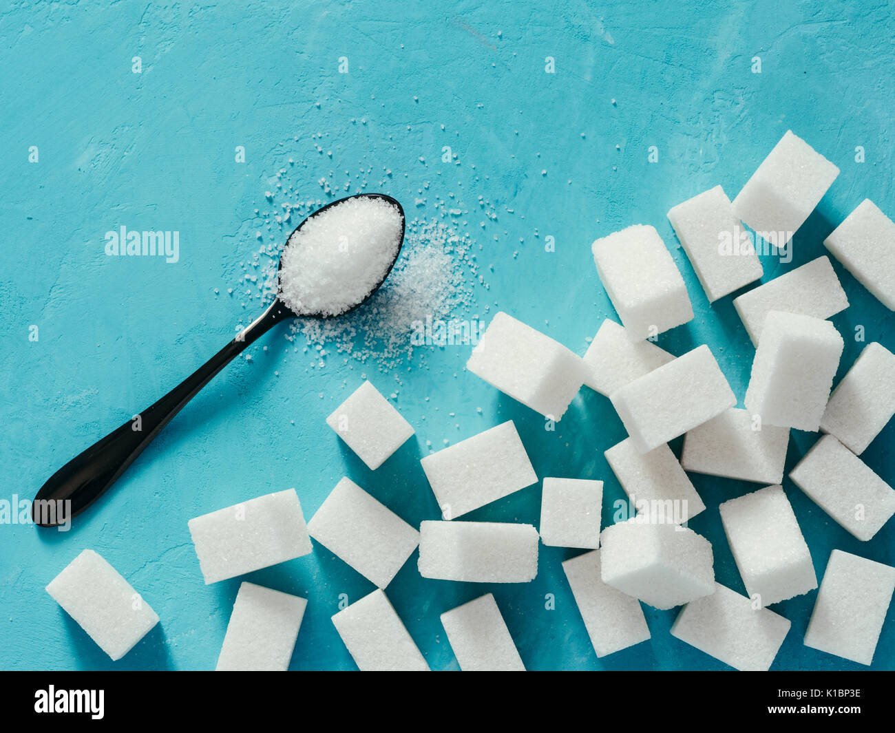 background of sugar cubes and sugar in spoon. White sugar on blue background. Sugar with copy space. Top view or flat lay Stock Photo