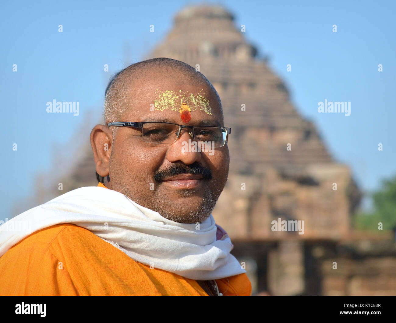 Well-built Hindu Brahmin priest with modern eyeglasses and traditional sikha haircut poses for the camera in front of Konark's Sun Temple. Stock Photo