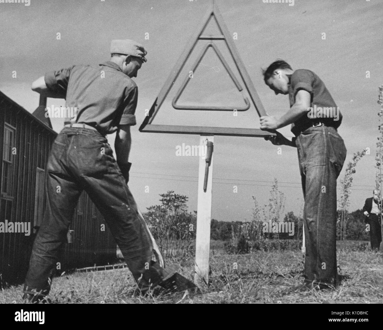 Two male Civilian Conservation Corps (CCC) workers in uniform erecting a sign in a field, one worker using a shovel, the other holding the sign to steady it, Beltsville, Maryland, 1935. From the New York Public Library. Stock Photo