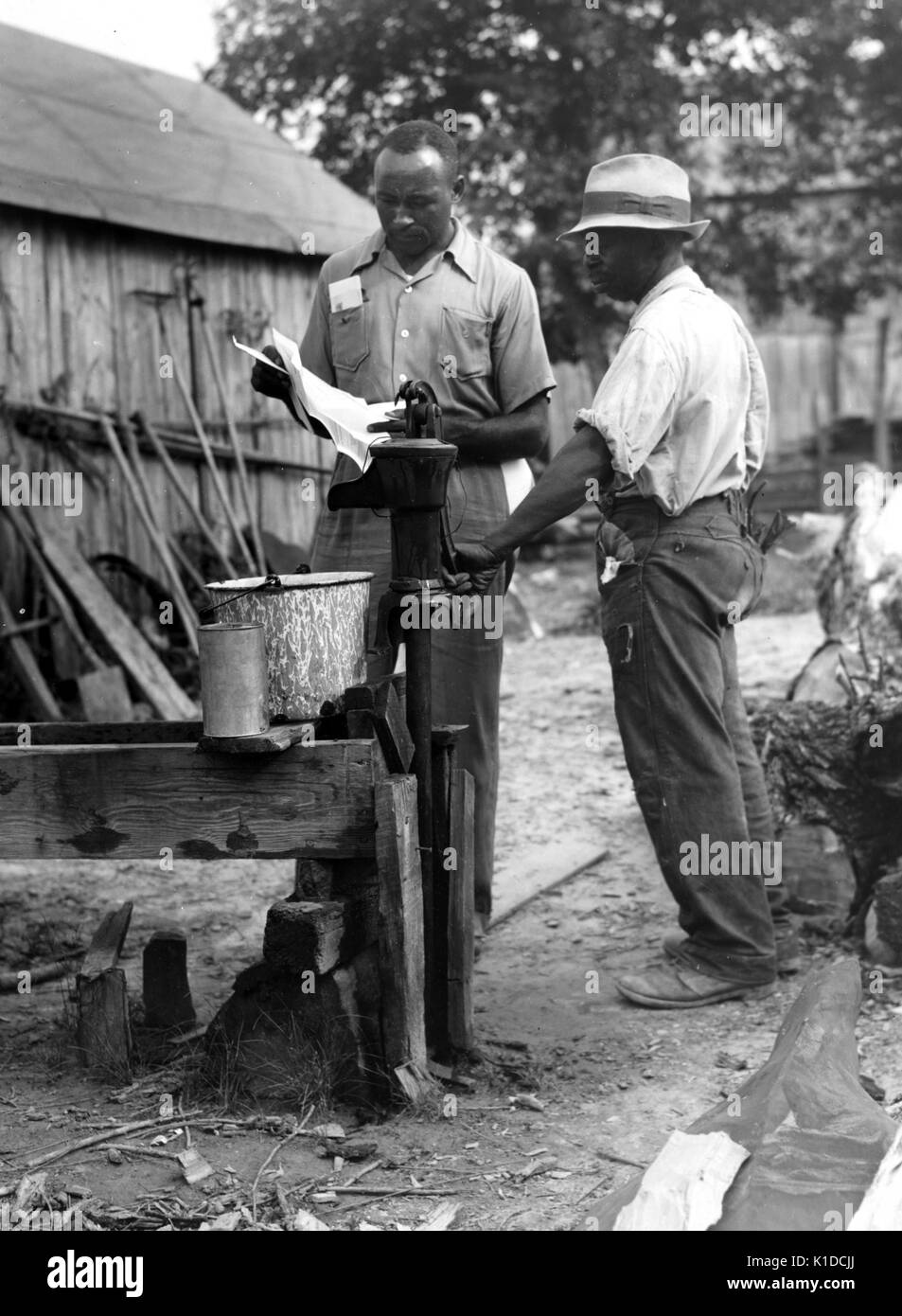An African-American Farm Security Administration supervisor consults with a borrower about unsanitary water supply, safe well demonstration, near La Plata, Maryland, 1900. From the New York Public Library. Stock Photo