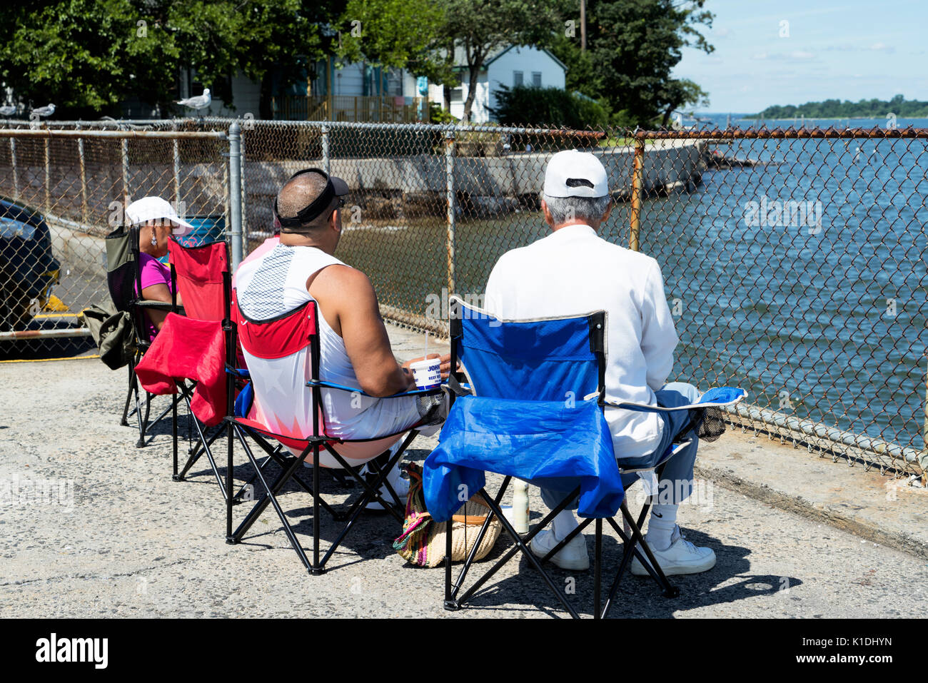 Bronx, New York, City Island.  Three Senior People Two Men, One Woman, Sitting on Folding Chairs, Socializing and Enjoying the View. Stock Photo