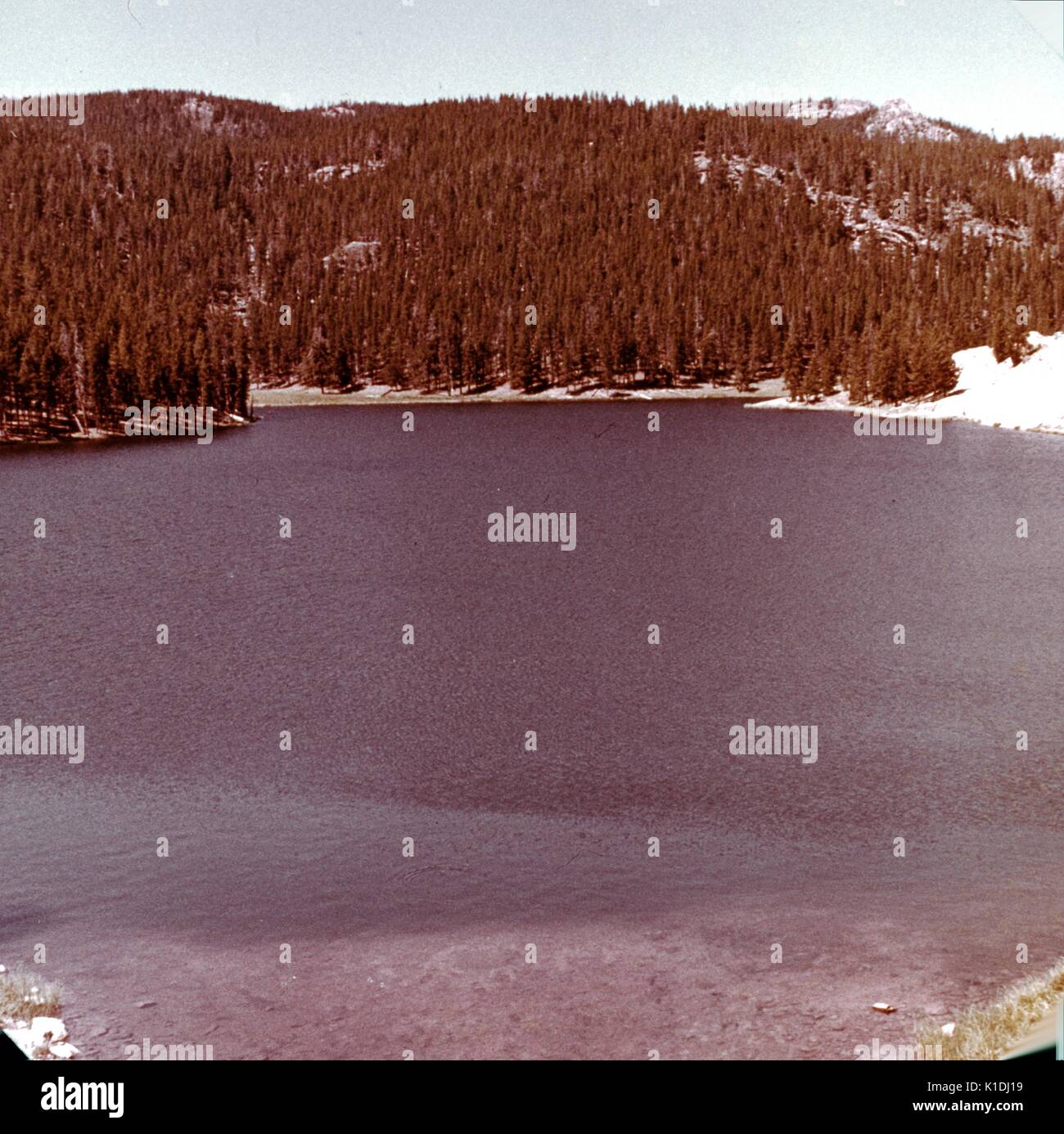 A photograph of Sibley Lake, taken from above on a hillside vantage point, snow can be seen covering the ground, trees and hills make up the background, Bighorn National Forest, Wyoming, 1975. Stock Photo