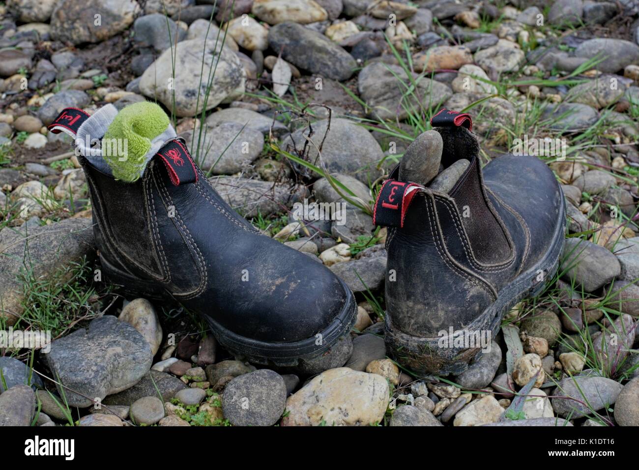 A dirty pair of child's redback work boots, abandoned on stony ground. Stock Photo