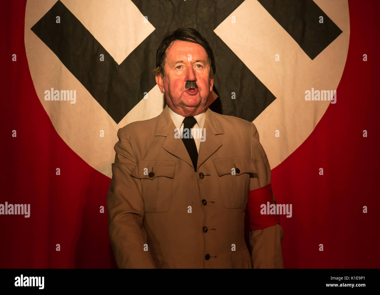 Pleasance Courtyard, Edinburgh, Scotland, United Kingdom, 26th August 2017. Pip Utton, versatile actor and Fringe Festival regular, in one man solo role of historical figure Adolf Hitler at Edinburgh Fringe Festival, Pleasance Courtyard, standing in front of a large banner with a swastika Stock Photo
