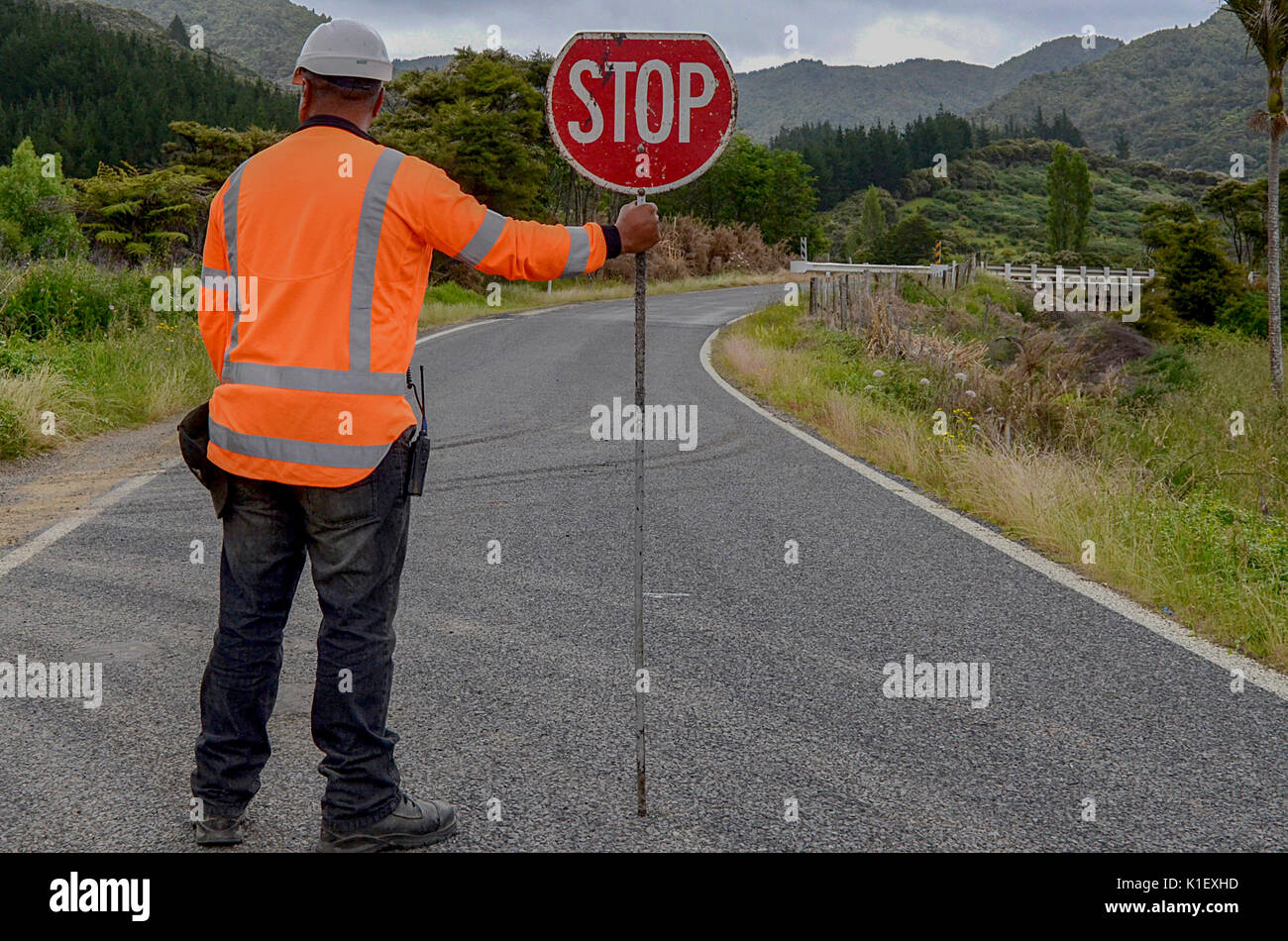 Man holding STOP sign. Man in red jacket on rural road. Stock Photo